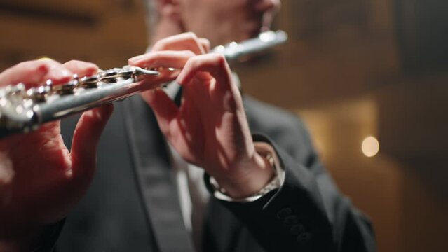 professional flutist is playing flute in philharmonic hall, rehearsal or concert of symphonic orchestra, closeup