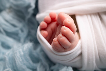 The tiny foot of a newborn. Soft feet of a newborn in a white blanket and on a blue background. Close up of toes, heels and feet of a newborn baby. Studio Macro photography. Woman's happiness
