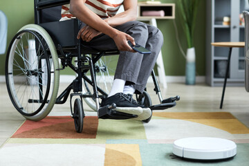 Cropped shot of modern man with disability using wireless robot vacuum cleaner in home interior, copy space