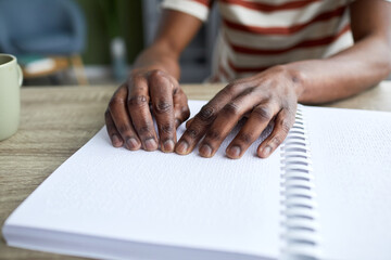 Closeup of blind African American man reading tactile book in braille, accessible education...