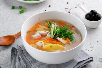 Chicken soup with vegetables and herbs in a white bowl served on the kitchen table