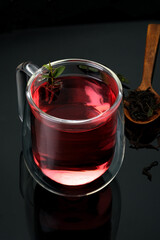 Red berry tea with mint in a glass with a wooden spoon and herbs on a black background