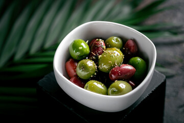 Fresh whole olives with herbs, spices and lemon in a white bowl. Antipasti or wine appetizer