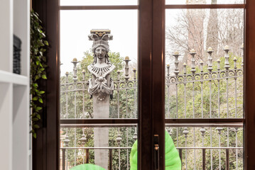 Window of an apartment overlooking a park with metal fence with sculptures of classic cut