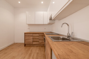 Newly renovated kitchen with wooden furniture, wooden countertop with black appliances and bright white upper cabinets and matching wooden floors
