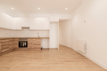 Newly renovated kitchen with wood cabinets, wood counter tops with black appliances and gloss white upper cabinets, plain white painted walls and matching wood flooring and white aluminum radiator
