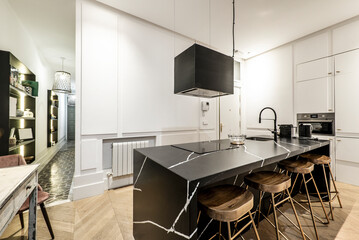 Island of a kitchen with modern decoration and furniture with black marble top, black hanging...