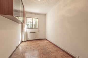 Empty living room with sintasol floors similar to parquet, window with bars and curtains and below an aluminum radiator and a cabinet with glass doors on the wall