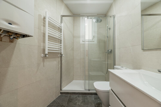 Newly renovated toilet with glass partition with sliding doors, white towel rail, polished marble walls and gray floors