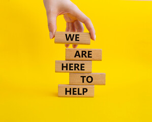 We are here to help symbol. Concept words we are here to help on wooden blocks. Beautiful yellow background. Business and we are here to help concept. Copy space.