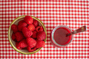 Small bowl with fresh raspberries next to a glass with raspberry jam.