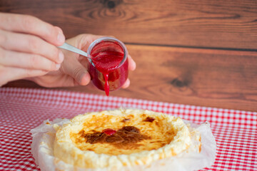 Man hand holding a teaspoon with raspberry jam, decorating a homemade cheesecake.
