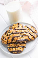 Chip cookies with peanuts and chocolate strips on white table.