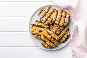 Chip cookies with peanuts and chocolate strips on white table.
