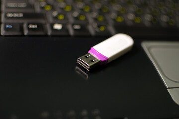 White USB Flash memory card lying on black laptop case in front of his keyboard. Virtual memory storage with USB output. Blurred keyboard