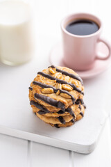 Chip cookies with peanuts and chocolate strips on white table.
