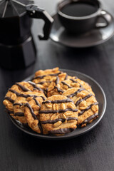 Chip cookies with peanuts and chocolate strips on plate on black table.