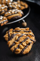 Chip cookies with peanuts and chocolate strips on black table.