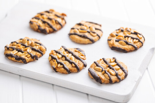 Chip cookies with peanuts and chocolate strips on white table.
