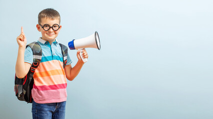 Little schoolboy with megaphone on blue background. Boy with megaphone making an announcement with...