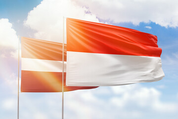 Sunny blue sky and flags of indonesia and latvia