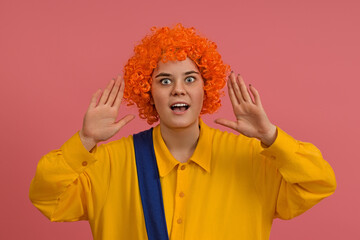 a smiling clown in a wig and a yellow-blue suit screams loudly and cheerfully, pressing his hands to his mouth on a colored background