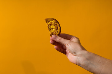 half a cookie in a human hand close-up on a yellow background