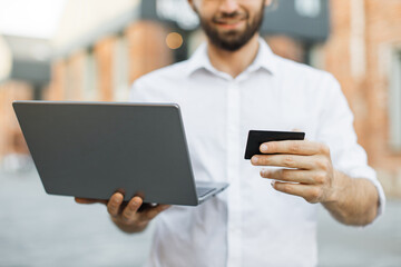 Focus on laptop and bank card. Business trip concept. Handsome young man, using notebook and holding credit card for shopping online. Male freelancer receive payment online.