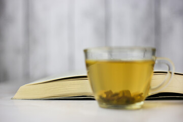 Brewed herbal green tea in a transparent cup in front of an open book on a light background.