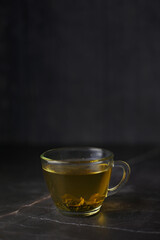 Illuminated brewed herbal green tea in a transparent cup on a dark background.