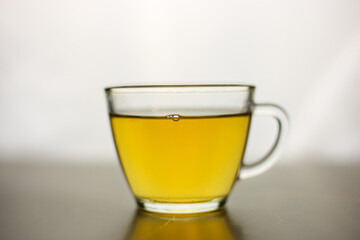 Brewed herbal green tea in a transparent cup on a dark table with a bright white light on the background