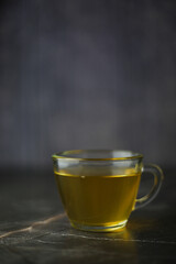 Illuminated brewed herbal green tea in a transparent cup on a dark background.