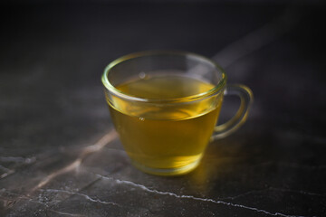 Illuminated brewed herbal green tea in a transparent cup on a dark background.