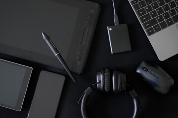 Stylus and graphics tablet with screen on black background next to headphones, laptop, computer...