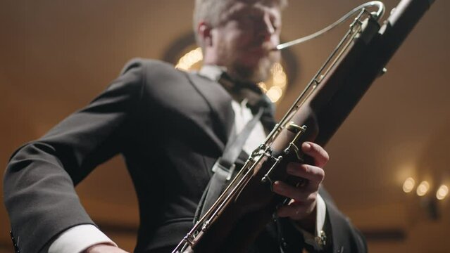 bassoonist with instrument on scene, musician is performing music by bassoon, symphonic orchestra
