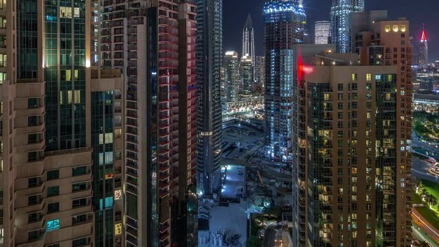 Aerial cityscape night timelapse with illuminated architecture of Dubai downtown. Many tall skyscrapers and towers with glowing windows. New construction site.