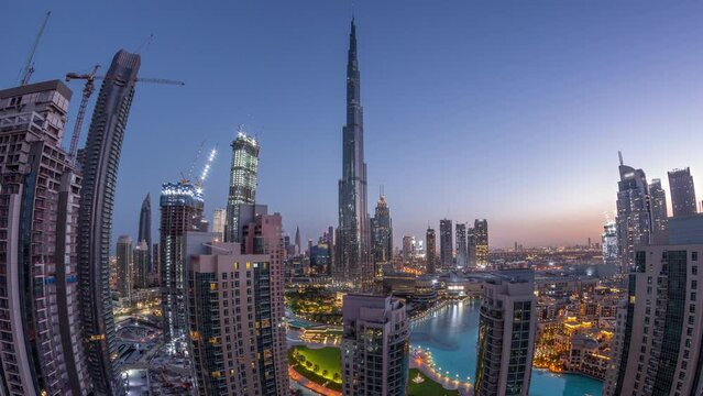 Panorama of Dubai Downtown cityscape with tallest skyscrapers around aerial night to day transition timelapse. Construction site of new towers and busy roads with traffic from above