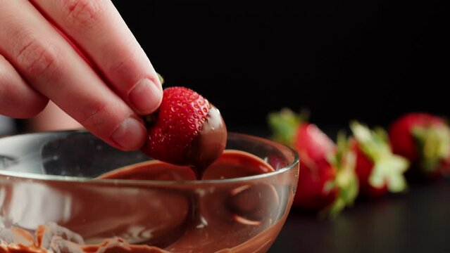 Strawberry in melted chocolate close-up, melting chocolate bar for fondue. Putting berries into choco mousse. Professional chef cooking cake dessert.
