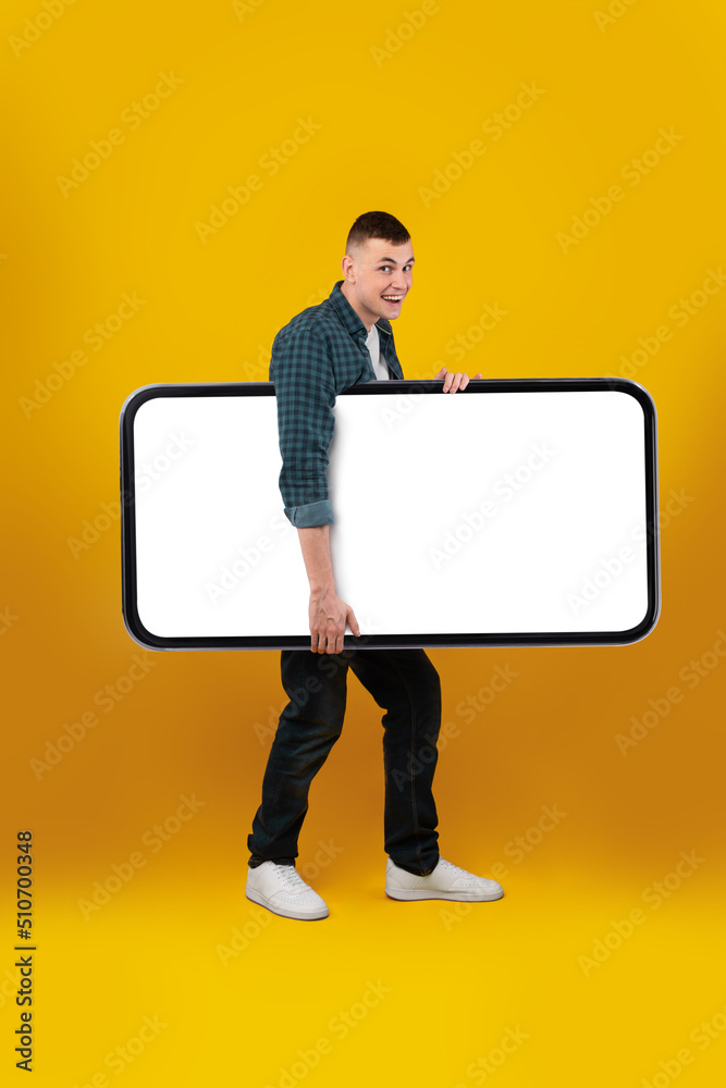 Poster man carrying huge cellphone empty screen on yellow background, vertical