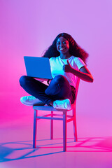 Full length of young black lady showing thumb up, using laptop, recommending remote studies or online work in neon light