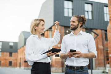 Happy man receiving keys from realtor woman at meeting, excited businessman purchasing real estate, making successful deal, attractive male buying first own dwelling, new apartment, mortgage or rent