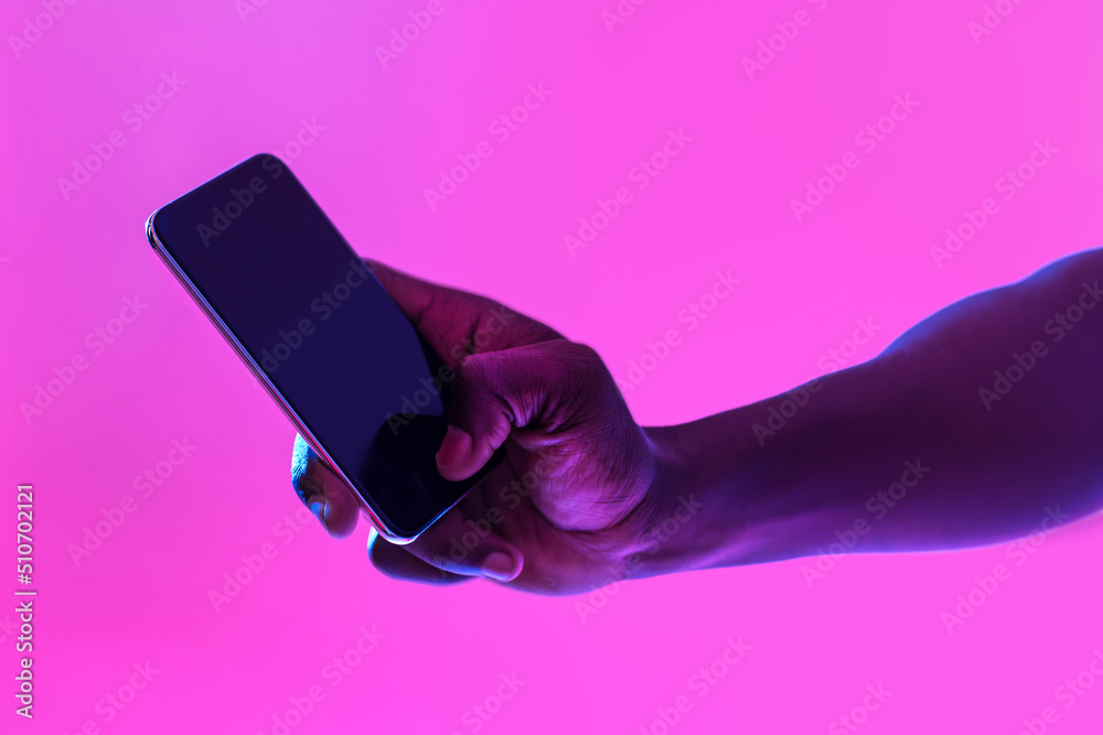 Poster unrecognizable black guy using cellphone with blank screen in neon light, free space for website or 