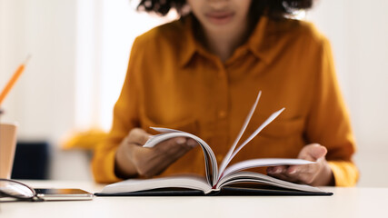 Education and free time. Young black woman reading book or writing notes in notepad, sitting at...