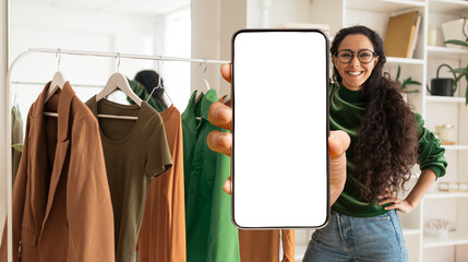Fashion App. Stylist Woman Showing Blank Smartphone While Standing Near Clothing Rail