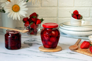 Homemade strawberry jam in glass jars with fresh strawberry on wooden boarding. Kitchen table decorated chamomiles with fresh strawberry jam, morning breakfast concept.