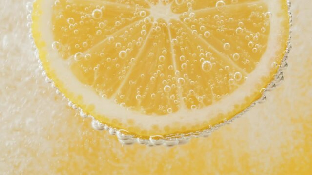 Lemon slice in carbonated water on yellow background, fizzy summer drink, making cocktail of citrus fruits, cold lemonade, ripe sliced fruit. 