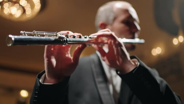 talented flutist is playing flute, portrait of musician in concert in old opera house or philharmonic hall