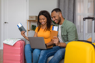 Family tours concept. Happy african american family with packed suitcases and passports with tickets, using laptop