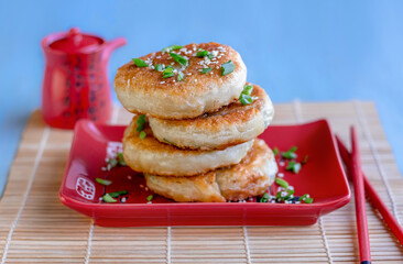 Stack of Sesame Flatbread with scallion filling on a plate with sauce bottle on background. Layer, rolled, crispy pancakes decorated with sesame and sliced spring onion. Selective focus, horizontal.