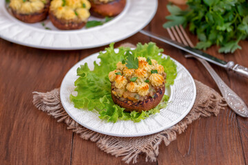 Vegan Stuffed Mushrooms with mashed potatoes filling. Large brown stuffed mushroom, portion on a plate. Wooden background, close up, selective focus.